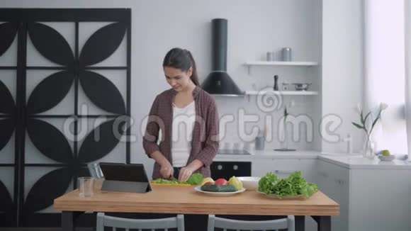 苗条的食物快乐的女孩切绿色的健康饮食沙拉午餐用药片和食谱在厨房的桌子上视频的预览图