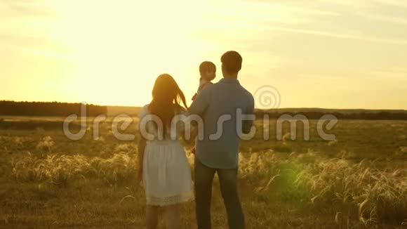 爸爸和妈妈带着她的小女儿在田野里的夕阳下抱着她的怀里散步家人和女儿一起玩视频的预览图