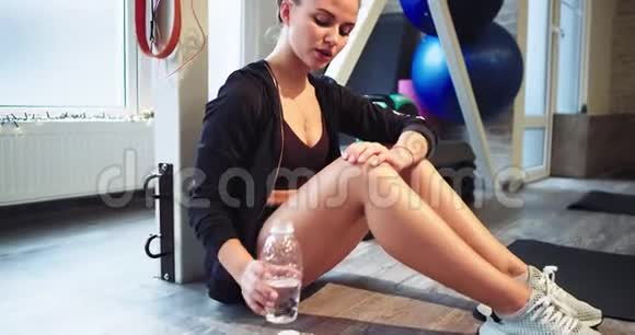 口渴的女士在健身房辛苦锻炼了一天后从塑料瓶里喝了些水她坐在地板上视频的预览图