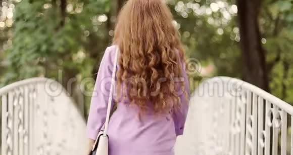 红色长发的快乐女孩正走在白色的桥上的夏季公园里视频的预览图