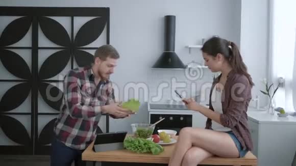 快乐的饮食快乐的女孩在手机上拍照有趣的家伙一边烹饪健康的食物作为午餐并制作视频的预览图