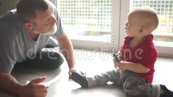 老人和婴儿坐在窗户对面的地板上玩爷爷和孙子男孩拿着眼镜视频的预览图