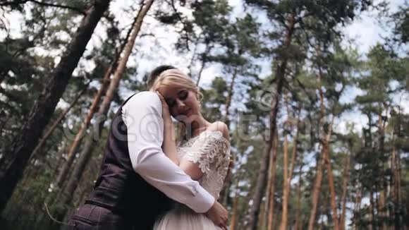穿着白色连衣裙的女孩把头按在男朋友胸前一对相爱的夫妇站在一棵美丽的松树中间视频的预览图