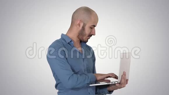 年轻的中东商人站在笔记本电脑上打字时他手里拿着梯度背景视频的预览图