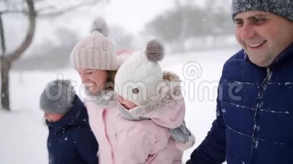 友好的全家人在降雪的情况下在冬天的森林里散步父亲母亲儿子和女儿视频的预览图