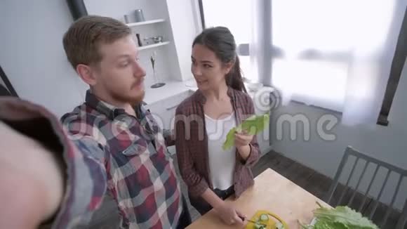 在厨房里一家人快乐年轻的女人和男人一起在手机上自拍同时烹饪健康饮食视频的预览图