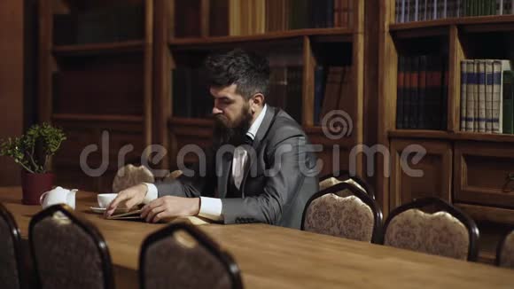 咖啡休息时间看书的人穿着经典西装的男士坐在复古的室内图书馆书架上视频的预览图
