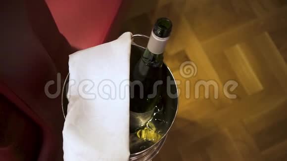 在棕色地板背景下用白色毛巾将打开的香槟瓶放入冰桶中房间服务理念视频的预览图