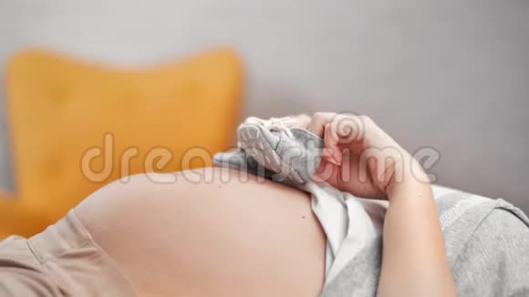 特写俏皮的女性手牵着可爱的婴儿鞋踩在大裸怀孕的肚子上视频的预览图