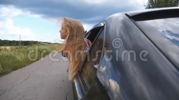 一个美丽的小女孩一头金色的长发斜倚在车窗外在阴云密布的乡间小路上视频的预览图