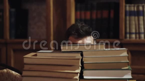 一个有趣的留胡子的人在图书馆的书堆之间有着快乐面孔的人背景上的书架有意思的是视频的预览图