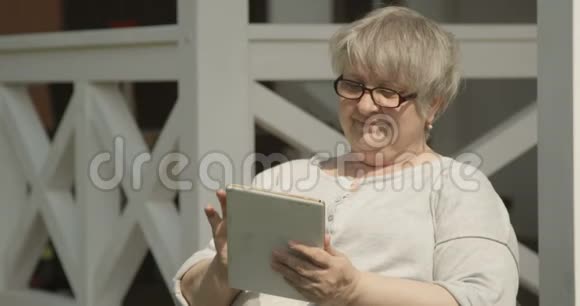 阳光明媚的一天在养老院拍摄的带有眼镜的平板电脑拍摄的老年妇女肖像视频的预览图