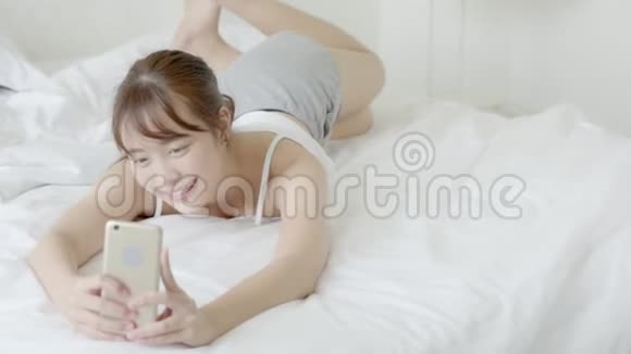 美丽的肖像年轻的亚洲女人躺在卧室里用智能手机自拍视频的预览图