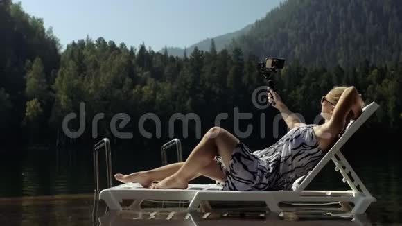 女性拍摄手持电影万向节稳定智能手机女孩躺在码头上晒太阳自拍博客视频的预览图