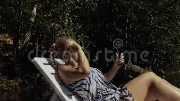 女性拍摄手持电影万向节稳定智能手机女孩躺在码头上晒太阳自拍博客视频的预览图