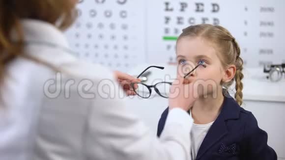 快乐的小女孩照镜子在医生的帮助下选择时尚的眼镜视频的预览图