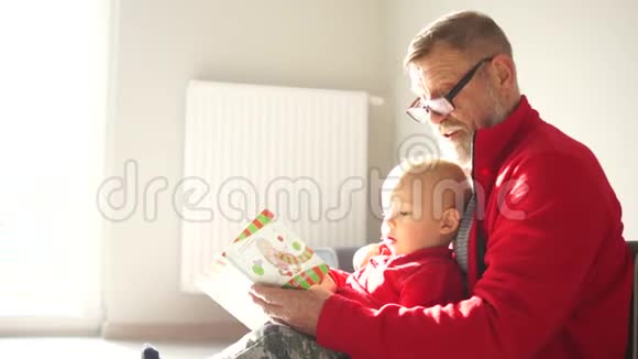爷爷给坐在窗前地板上的小孙子读一本书祖父和孙子视频的预览图