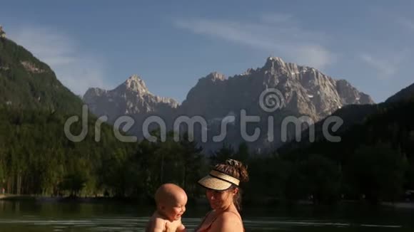 妈妈和宝宝在一个温暖的山湖里游泳在高高的雪山上母亲日旅游理念幸福家庭视频的预览图
