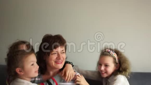 可爱的好祖母和她的四个孙子孙女坐在沙发上拥抱带着女保姆视频的预览图