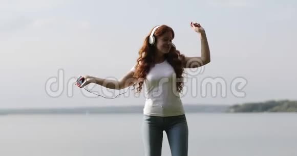 戴着白色耳机的红发女孩正在手机上听歌和跳舞视频的预览图