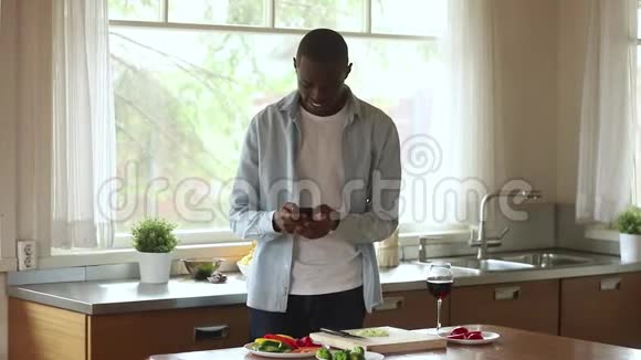 快乐的非洲男人使用智能手机手机应用程序烹饪厨房视频的预览图