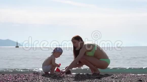 年轻的妈妈和宝宝慢慢地在海边的沙滩上堆起沙像视频的预览图