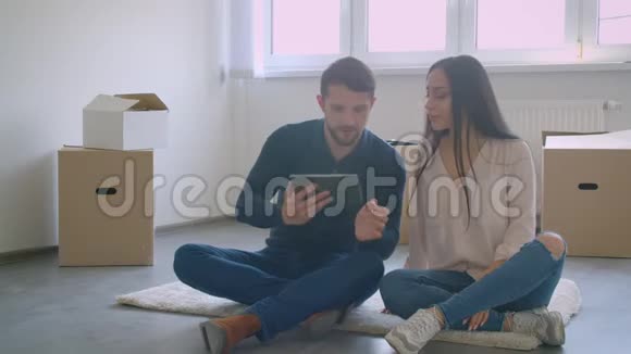 美丽的白种人夫妇使用数字平板电脑交谈和微笑而坐在地板附近的纸箱视频的预览图