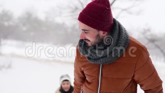 可爱的夫妇在下雪的冬天滑雪下雪时男人和女朋友拉雪橇女人玩得开心视频的预览图