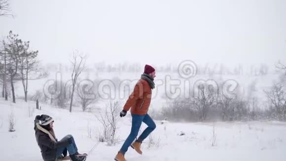 可爱的夫妇在下雪的冬天滑雪下雪时男人和女朋友拉雪橇女人玩得开心视频的预览图