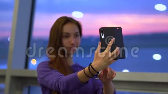 年轻女孩在机场窗口附近的手机上自拍照片视频的预览图