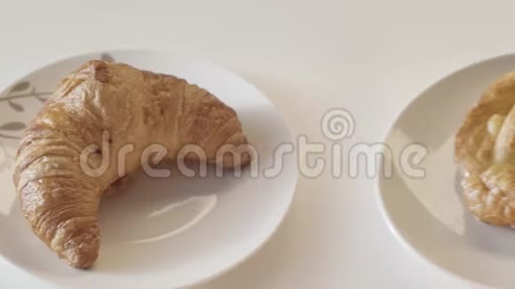 将刚烤好的牛角面包和甜面包放在白色桌子背景上的陶瓷盘子上股票视频的预览图