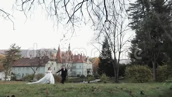 一对穿着婚纱的情侣散步一对夫妇在树之间散步新娘的婚纱结婚舞会婚礼视频的预览图