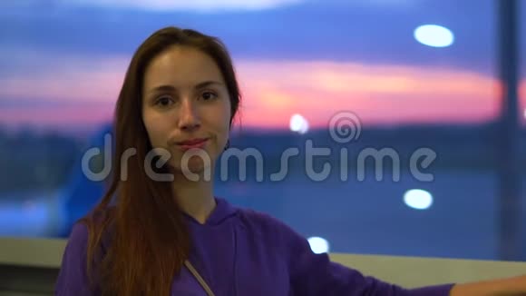 日出时年轻美丽的微笑女孩站在机场的窗前视频的预览图