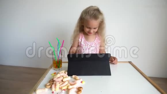 孩子金发女孩穿着粉红色的光滑连衣裙玩平板电脑万向节运动视频的预览图