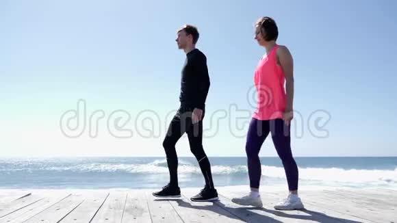 年轻的运动男女在海滩上伸展后地面的海浪慢动作视频的预览图