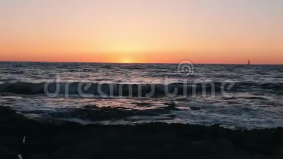 美丽的海上日落小船在地平线上小船漂浮在海上迎着橙色的夕阳日落时难以置信的海浪视频的预览图
