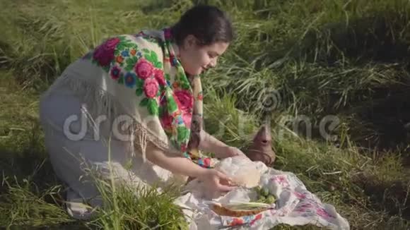 美丽的超重女人坐在野草中拿着面包和土罐准备吃传统视频的预览图