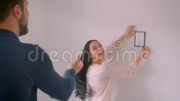 白种人快乐的女孩挂在白色的墙上而她的男朋友引导她到正确的地方视频的预览图