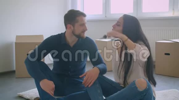 年轻的白种人夫妇坐在新房子的地板上靠近卡片盒玩钥匙和接吻视频的预览图