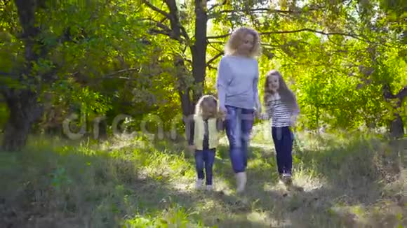 快乐的白种人一家人在秋天的公园里散步微笑着的成年卷毛女人牵着她漂亮的小手视频的预览图