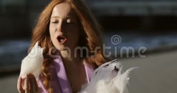 红发的快乐女孩正在日落时在夏季公园吃棉花糖视频的预览图