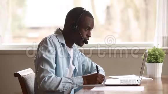 专注的非洲商人戴耳机看笔记本电脑做笔记视频的预览图