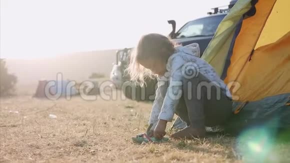 可爱的女孩子在探险营的旅游帐篷附近穿上鞋子视频的预览图
