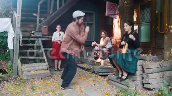 一个长胡子的男人跳着俄罗斯民族舞蹈女人坐在乡间别墅附近的楼梯上看着他一个女人视频的预览图