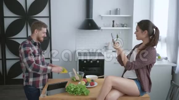 快乐的女孩坐在桌子上用手机拍照有趣的家伙一边做饭为早午餐做有用的饭视频的预览图