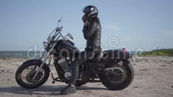可爱的白种人女人穿着黑色皮夹克和头盔坐在摩托车上女孩摘下头盔并伸直视频的预览图