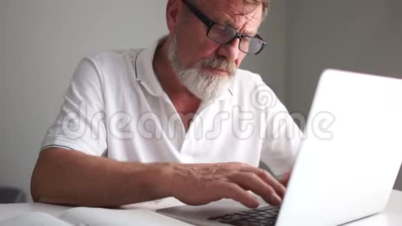 爷爷戴着眼镜留着灰色胡子忙着靠近笔记本电脑盯着屏幕打字成熟的男人和电脑视频的预览图