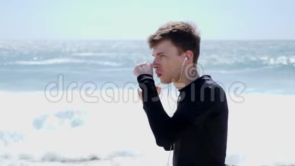 年轻的白种人运动员戴着耳机在空中打拳在海滩上拳击练习慢动作视频的预览图