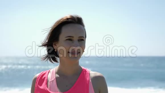 年轻美丽的白种人女子肖像微笑的相机站在海滩上慢动作视频的预览图