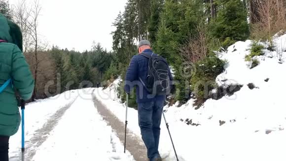 一名中年妇女和一名身穿夹克衫的男子在冬季沿着一条带有北欧步行杆的森林道路行走这是一种运动的概念视频的预览图